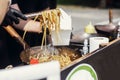 Chef putting noodles in carton box to go from pan on fire at open kitchen. Fried chinese japanese noodles with vegetables and Royalty Free Stock Photo