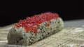 Chef Putting Roe red Sushi Caviar On Top Of Shrimp Tempura Sushi Roll With Avocado Slices Using A Teaspoon - close up