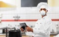 Chef in respirator with tablet pc at kitchen