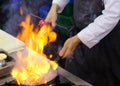 Chef in restaurant kitchen at stove with pan, doing flambe on food Royalty Free Stock Photo