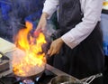 Chef in restaurant kitchen at stove with pan, doing flambe on food Royalty Free Stock Photo