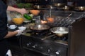 Chef in restaurant kitchen at stove with pan, doing flambe on food. low ligth selective focus. Royalty Free Stock Photo