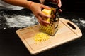 Chef rubs fresh fragrant cheese on a grater for making homemade italian pizza on a wooden cutting board