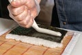 The chef`s hand squeezes cream cheese onto a piece of rice and nori