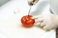 Chef's hands gloved in latex slicing a ripe tomato