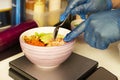 Chef\'s hands gloved in plastic preparing a salmon poke bowl with masago roe and avocado