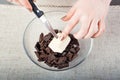 The chef`s hands hold a piece of butter on a knife over a bowl of chocolate