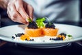 Chef& x27;s hands meticulously garnish gourmet dish of salmon rolls topped with caviar on a white plate