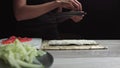 Chef`s hands sprinkle sesame seeds on the inside out sushi. Japanese chef in black gloves at work preparing sushi roll