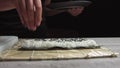 Chef`s hands sprinkle sesame seeds on the inside out sushi. Japanese chef in black gloves at work preparing sushi roll