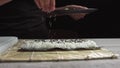 Chef`s hands sprinkle sesame seeds on the inside out sushi. Japanese chef in black gloves at work preparing sushi roll