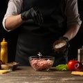 Chef salting minced meat to create a burger patty. Against the background with ingredients for a burger. Gastronomy, recipes, Royalty Free Stock Photo