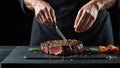 Chef is salting or seasoning raw ribeye steak laying on graphite serving board