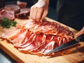 Chef Slicing Prosciutto on Wooden Board for charcuterie board. ?hef\'s hands with sliced prosciutto ham on a wooden
