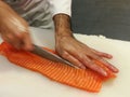 Chef slicing a raw fresh salmon fillet with a sharp knife on a white cutting board Royalty Free Stock Photo