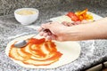 Chef smearing pizza over pizza dough with ketchup.