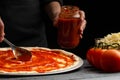 Chef smears Italian pizza with sauce, on black background, close-up. With ingredients mazzarella cheese, olives and tomato Royalty Free Stock Photo