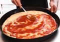 Chef spreading tomato paste onto a pizza base