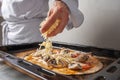 The chef sprinkles cheese on the vegetarian pizza