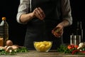 The chef sprinkles french fries with herbs on a background with vegetables. Making tasty but harmful food. Background for design Royalty Free Stock Photo