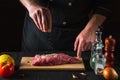 Chef sprinkles the raw beef meat with salt. Preparing meat before baking. Working environment in kitchen of restaurant or cafe Royalty Free Stock Photo