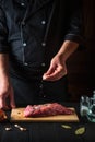 Chef sprinkles the raw beef meat with salt. Preparing meat before baking. Working environment in kitchen of restaurant or cafe Royalty Free Stock Photo