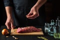 The chef sprinkles raw meat with salt. Preparing beef meat before baking. Working environment in the kitchen of restaurant or cafe Royalty Free Stock Photo