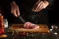 Chef sprinkles salt on raw fresh meat. Preparing lamb steak before baking. Working environment in a restaurant or hotel kitchen Royalty Free Stock Photo