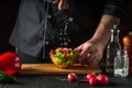 Chef sprinkles salt salad of fresh vegetables on wooden table. Preparing healthy food on the kitchen Royalty Free Stock Photo