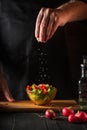 Chef sprinkles salt salad of fresh vegetables on wooden table. Preparing healthy food on the kitchen. Vertical image Royalty Free Stock Photo