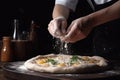 Chef sprinkling flour on pizza on black background, In a close-up view, the hands of a chef skillfully assemble a delicious