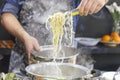 Chef takes out with slotted spoon hot steaming egg noodles from the pan Royalty Free Stock Photo