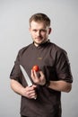 A chef in a uniform jacket shows off a professional chef`s knife and a tomato