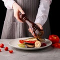 Chef using pepper mill. grilled vegetables and fish. pepper. female hands of the chef. on a black background Royalty Free Stock Photo