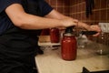 Chef using seamer or special seaming key, closes lids of jars with freshly canned tomato sauce, passata. Preserving food Royalty Free Stock Photo