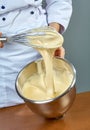 Chef whips yellow cream in a bowl by hand for making cheesecakes