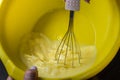 Chef with a whisk whips the pancake dough in a yellow plastic bowl