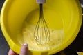 Chef with a whisk whips the pancake dough in a yellow plastic bowl