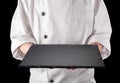 Chef in white uniform is holding an empty black slate serving plate. Black background Royalty Free Stock Photo