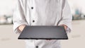 Chef in white uniform is holding an empty black slate serving plate. Black background Royalty Free Stock Photo