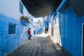 Chefchaouen, Morocco - APRIL 30 2019: View of a narrow street with a teenager moroccan boy leaning on a blue wall, bright sunny