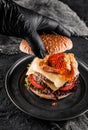 Chefs hand in black glove cooking the double hamburger or beef burger with red caviar, breaded shrimps, cheese, tomatoes,lettuce Royalty Free Stock Photo