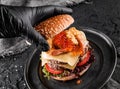 Chefs hand in black glove cooking the double hamburger or beef burger with red caviar, breaded shrimps, cheese, tomatoes,lettuce Royalty Free Stock Photo