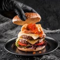 Chefs hand in black glove cooking the double hamburger or beef burger with red caviar, breaded shrimps, cheese, tomatoes,lettuce Royalty Free Stock Photo