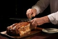 Chefs hands slicing a large pork roast on a wooden cutting board in the kitchen