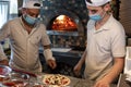 Chefs preparing pizza in a pizzeria wearing masks and protections during covid or coronavirus emergency