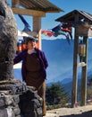 Full Potrait of a old Bhutanese woman in traditional dress beside the religious spinning wheel at Chele la , Paro, Bhutan