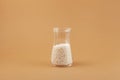 Chemical fertilizer in glass flask on brown background. Small white balls. Agricultural economics. Selective focus, copy space