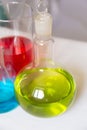 Chemical flasks with colored chemicals in tubes and flasks. Round capacity with green beverage inside. Selective focus, vertical