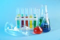 Chemical glassware with colorful samples and lab goggles on color background